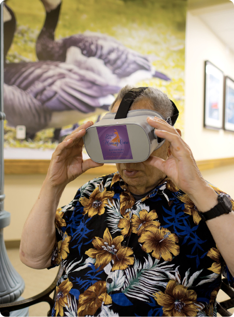 A person in a floral shirt uses a virtual reality headset indoors with a large bird mural in the background.