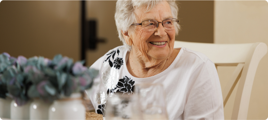 A smiling person with glasses sits at a table adorned with a bouquet of flowers in jars, radiating warmth and contentment.