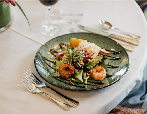 A green plate with shrimp and salad on a table, accompanied by wine glasses and silver cutlery, set atop a white tablecloth.