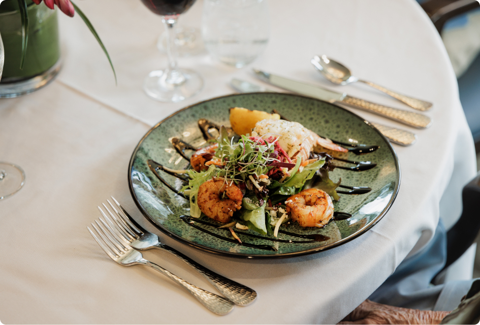 A delicious seafood dish with shrimp, greens, and garnish on a green plate, displayed on a white tablecloth with elegant tableware.