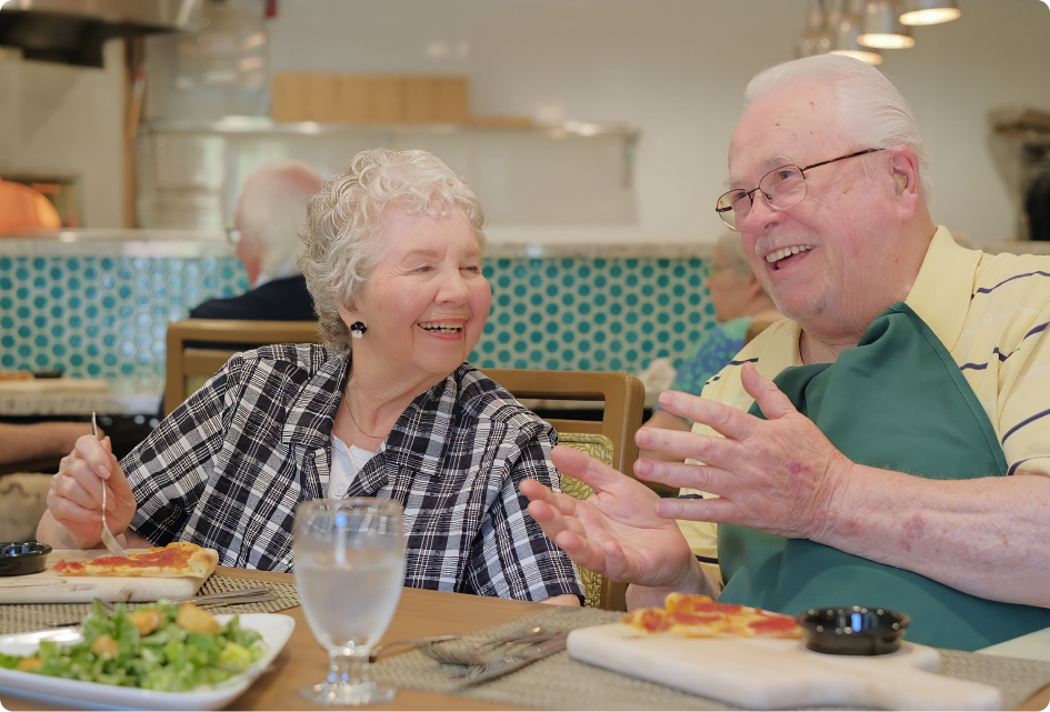 Two people happily sharing a meal at a cozy restaurant. Bright atmosphere with a patterned wall in the background and fresh salad on table.