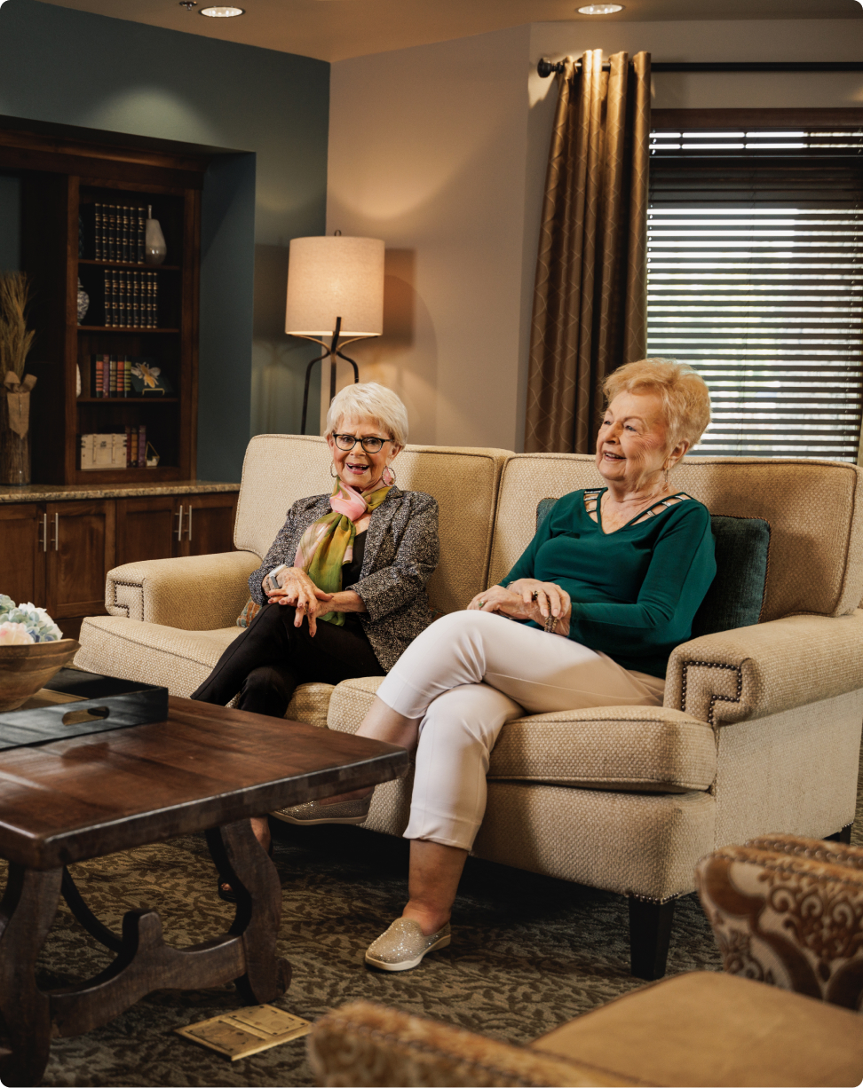 Two people sitting on a beige sofa in a cozy, well-decorated room with warm lighting and wooden accents.