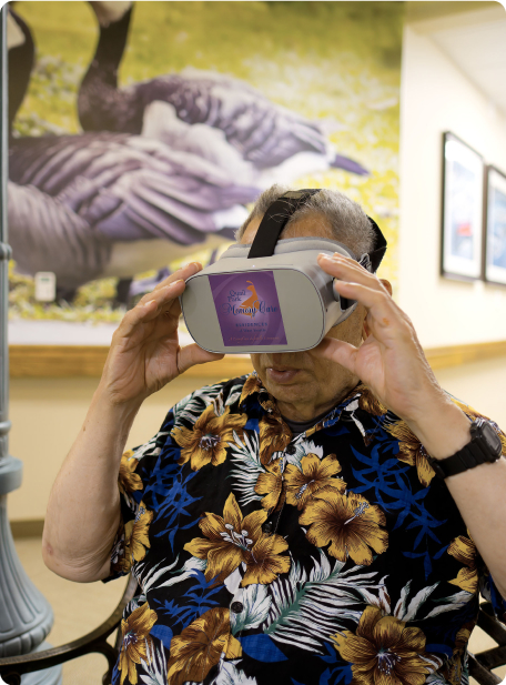 A person wearing VR goggles with a tropical shirt sits indoors. A large bird image decorates the wall in the background.