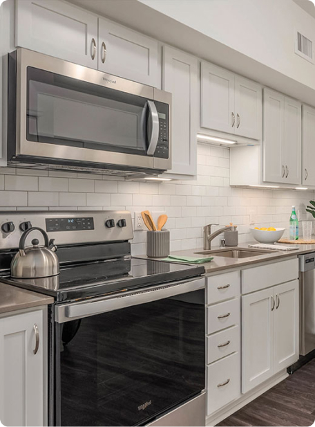 A modern kitchen features stainless steel appliances, white cabinets, and a tiled backsplash. A kettle and utensils are arranged neatly on the countertop.